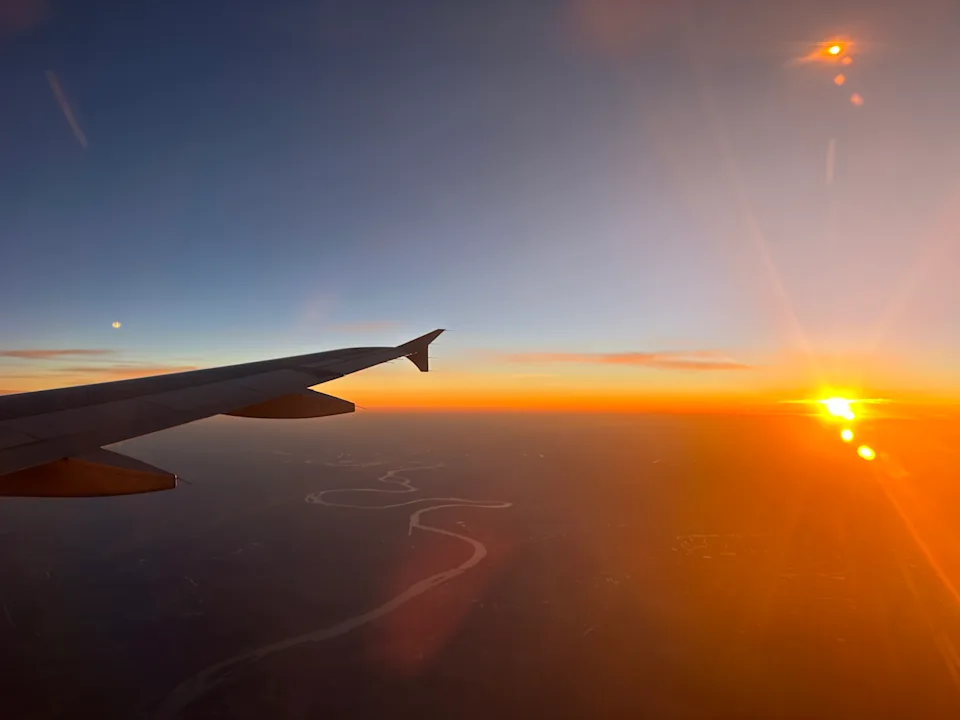 An airline wing as seen from a window at sunset