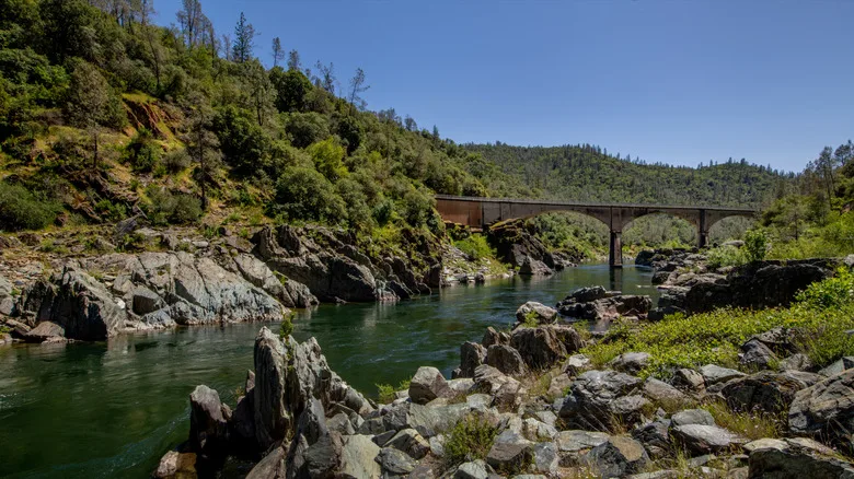 A stone arch bridge strides over the American River beside rocky outcrops and tree lined gorges