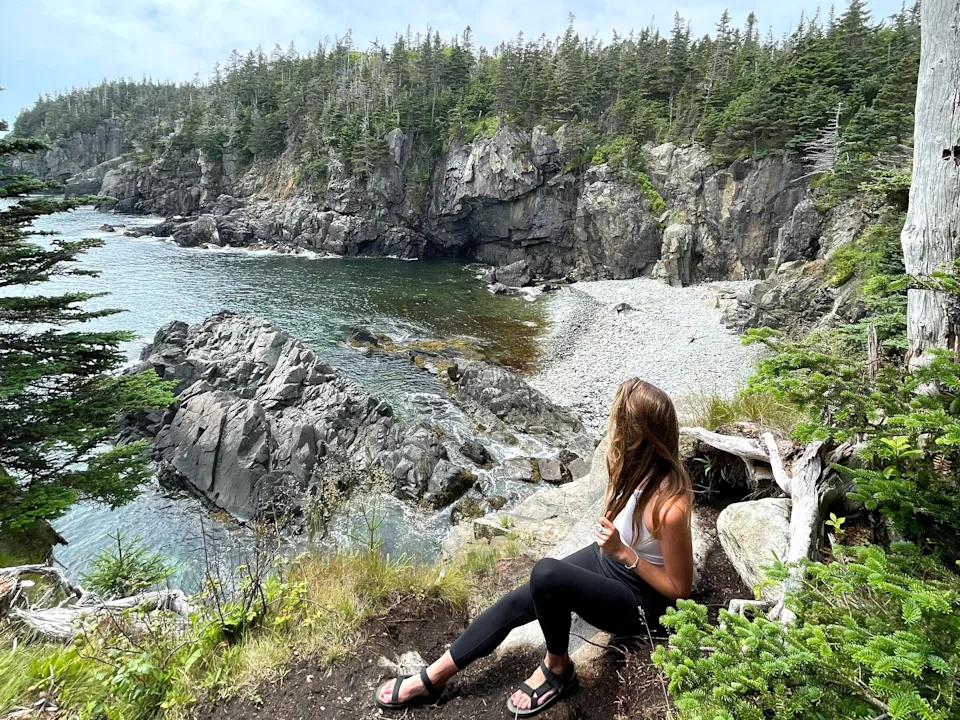 Emily sits on a rock, looking out at a body of water surrounded by tree-covered cliffs.