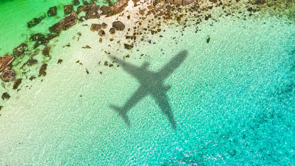 Aerial view of passenger plane silhouette and sandy beach blue sea with waves at sunset Summer vacation sea travel concept
