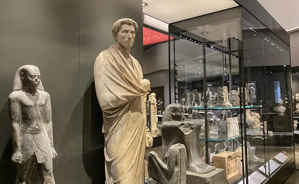 Museum display of ancient statues in glass cases, showcasing various historical sculptures in a gallery setting