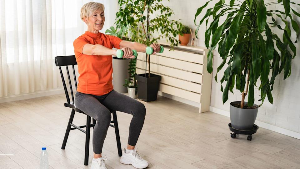  A senior woman lifting dumbbells from a chair. 