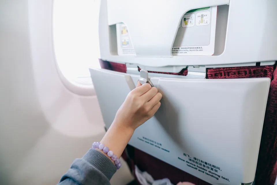 Close-up of a traveler adjusting the seatback tray on an airplane during flight