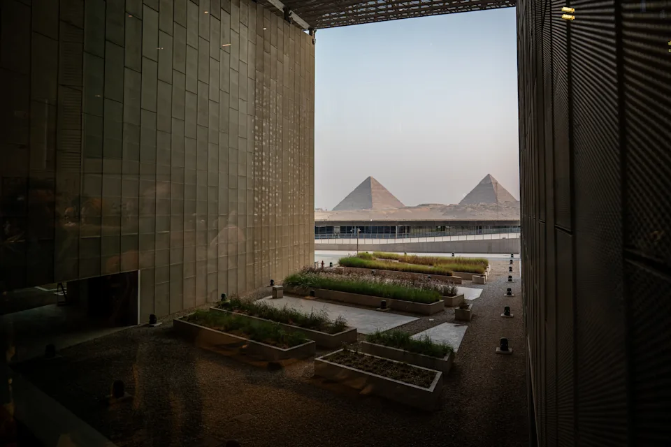 View of the Pyramids of Giza framed by modern architecture, with planters and pathways in the foreground under a clear sky
