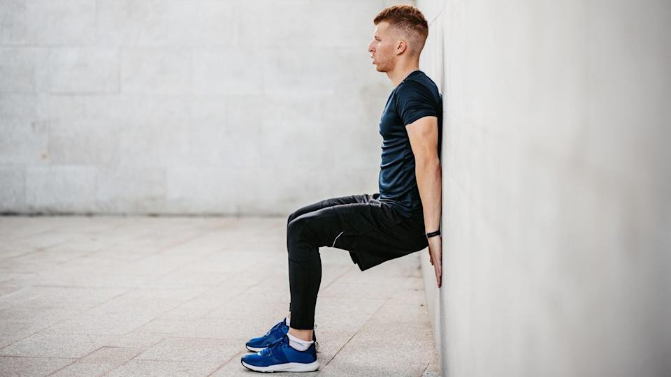  Man performing wall squat outdoors. 