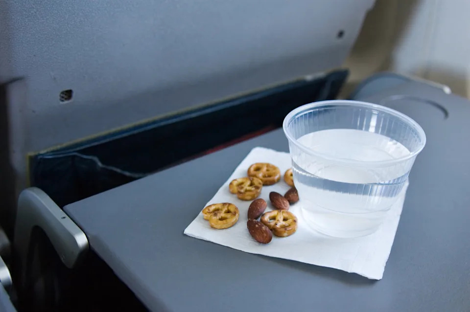 A cup of water and pretzels on an airplane tray table