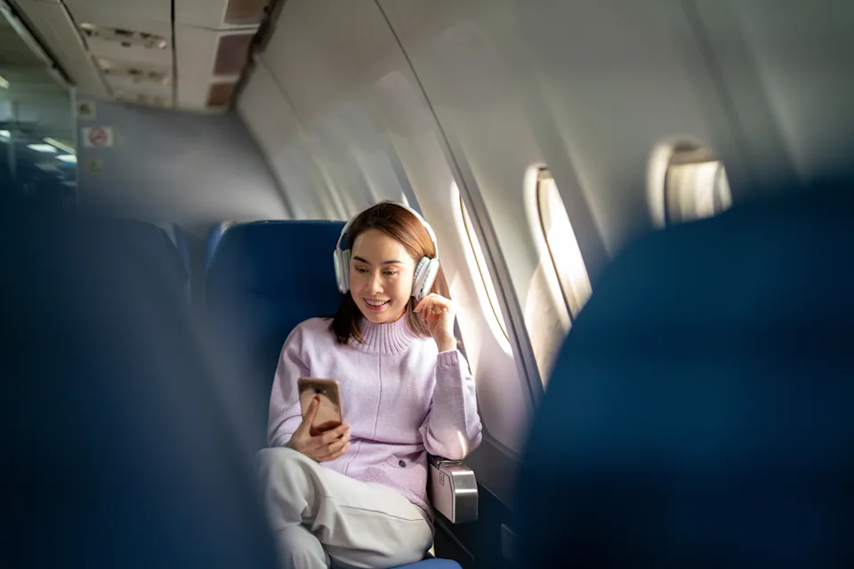 A woman passenger is happily using her smartphone while traveling on a flight, staying connected and entertained during the journey