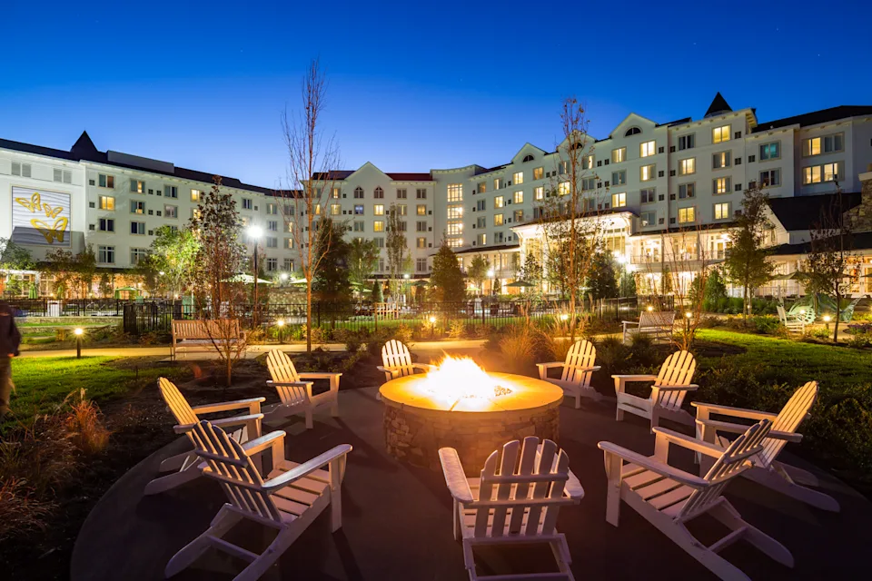 A fire pit surrounded by wooden Adirondack chairs in front of Dollywood DreamMore Resort and Spa at night