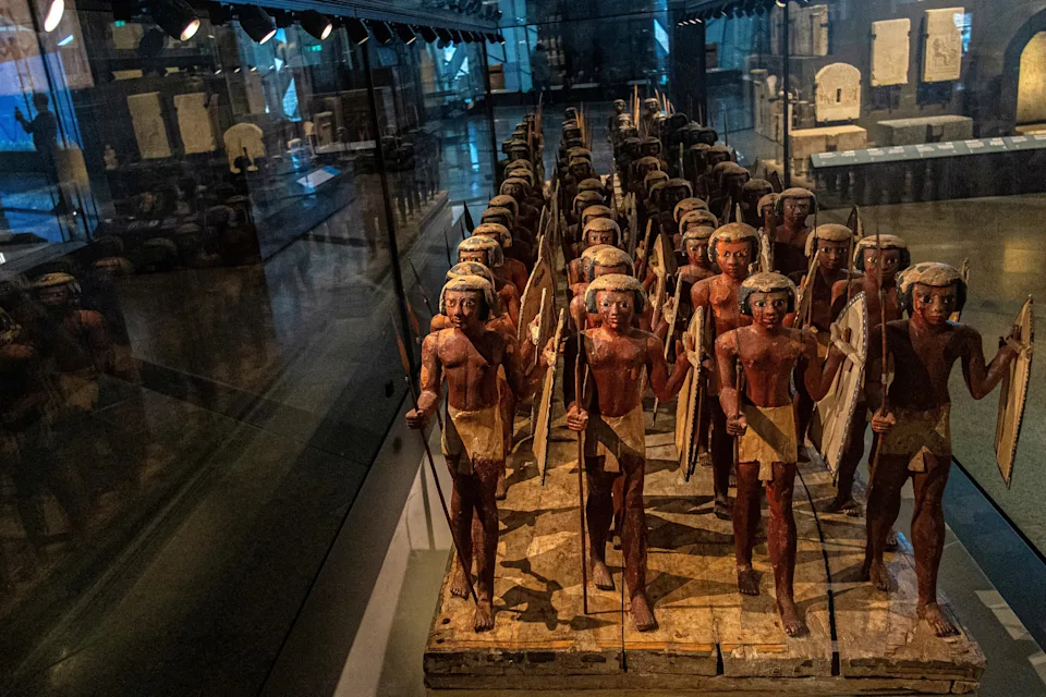 Ancient Egyptian wooden model depicts rows of soldiers holding weapons, displayed in a museum exhibit