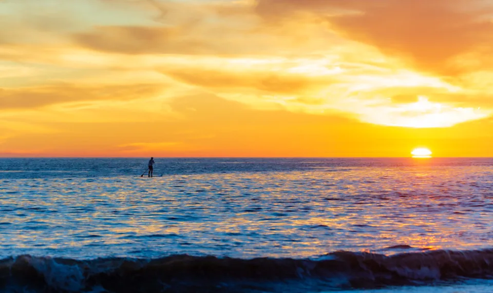 a woman paddleboards on the ocean at sunset in santa barabara california