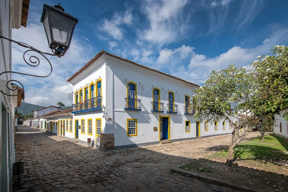 View of the exterior of Sandi Hotel, a charming white building on a cobblestone street, with blue sky and clouds above. - Courtesy of the Sandi Hotel 