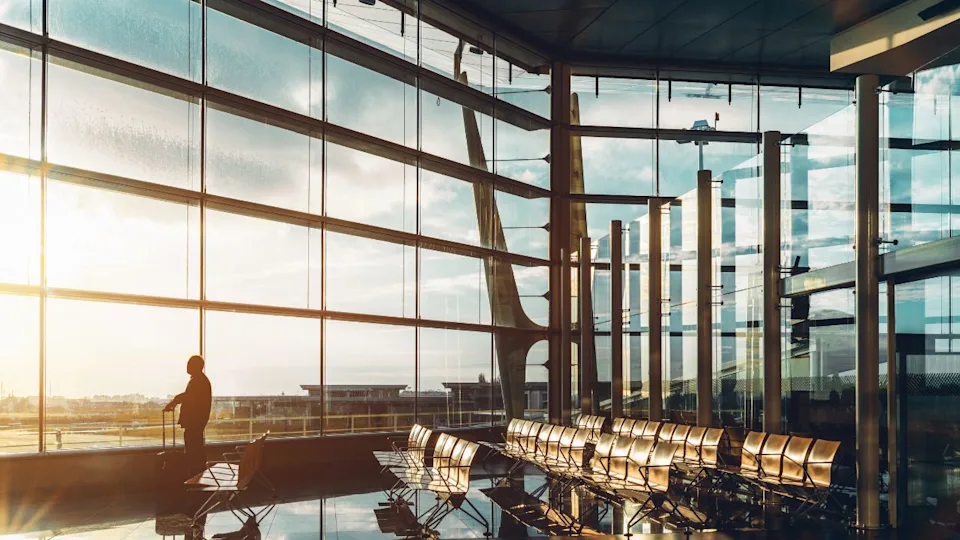 PORTO, PORTUGAL - JANUARY 13, 2017: Tall glass and metal waiting hall of modern airport terminal with silhouette of man looking through the window while standing with his bag near empty rows of seats