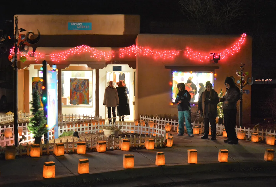 Farolitos glow on Canyon Road as people walk into festively lighted art galleries