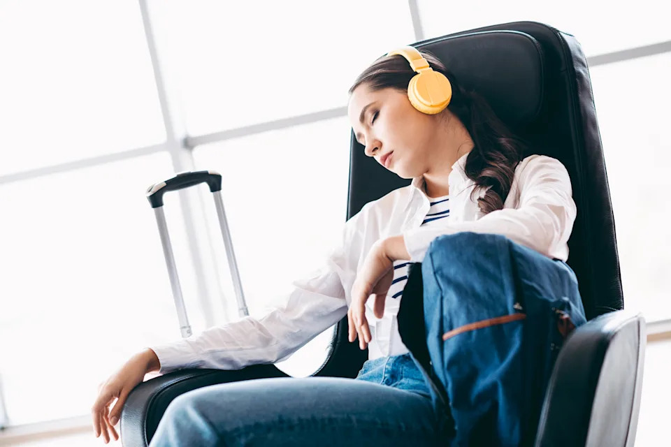 A young woman in casual attire sitting in an airport lounge with a suitcase and headphones, relaxing during travel.