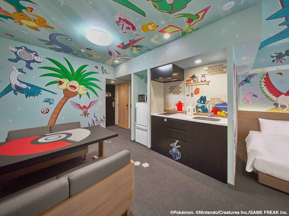 Hotel room with Pokémon-themed decor, featuring lively wall art and a cozy space with a kitchenette and bed
