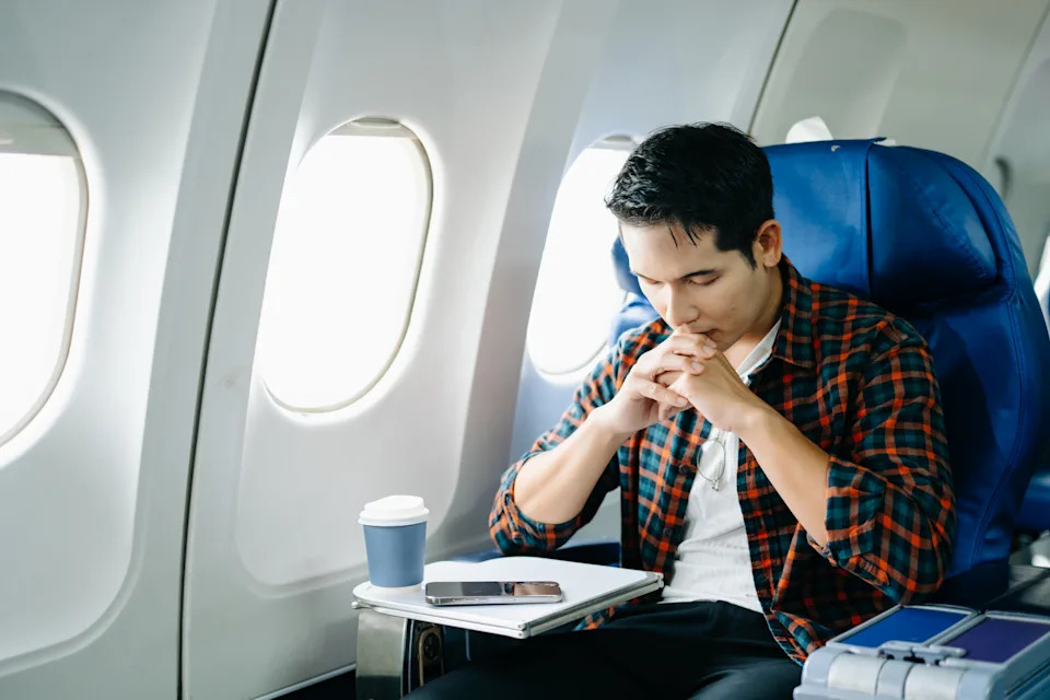 Travel stress, jet lag, or motion sickness. Young man with a headache or fatigue during a long flight. Tired passenger on a business trip. Pain, sit, air, mobile.
