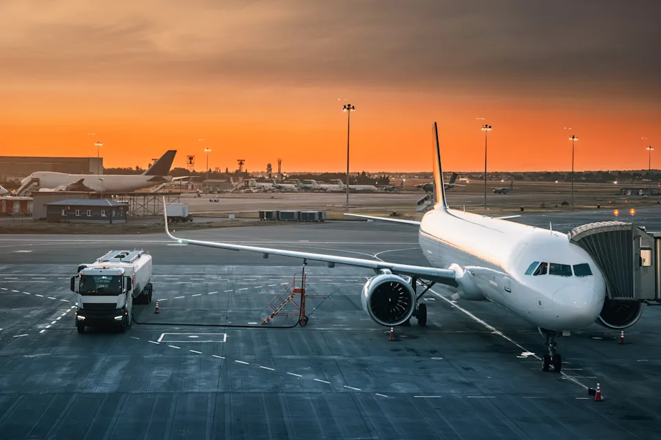 Tank truck refueling an airplane on the airport runway during a stunning sunset, casting warm hues across the evening sky