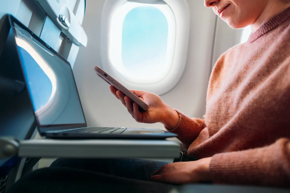 A professional utilizing their smartphone and laptop during an airplane journey, showcasing mobility and efficient connectivity for work or leisure activities while traveling.