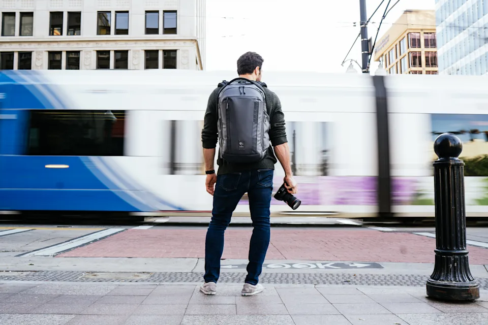 A man standing in a city carrying DSLR and Nomatic camera bag.