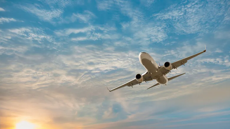 Airplane flying in a lightly cloudy blue sky at sunset