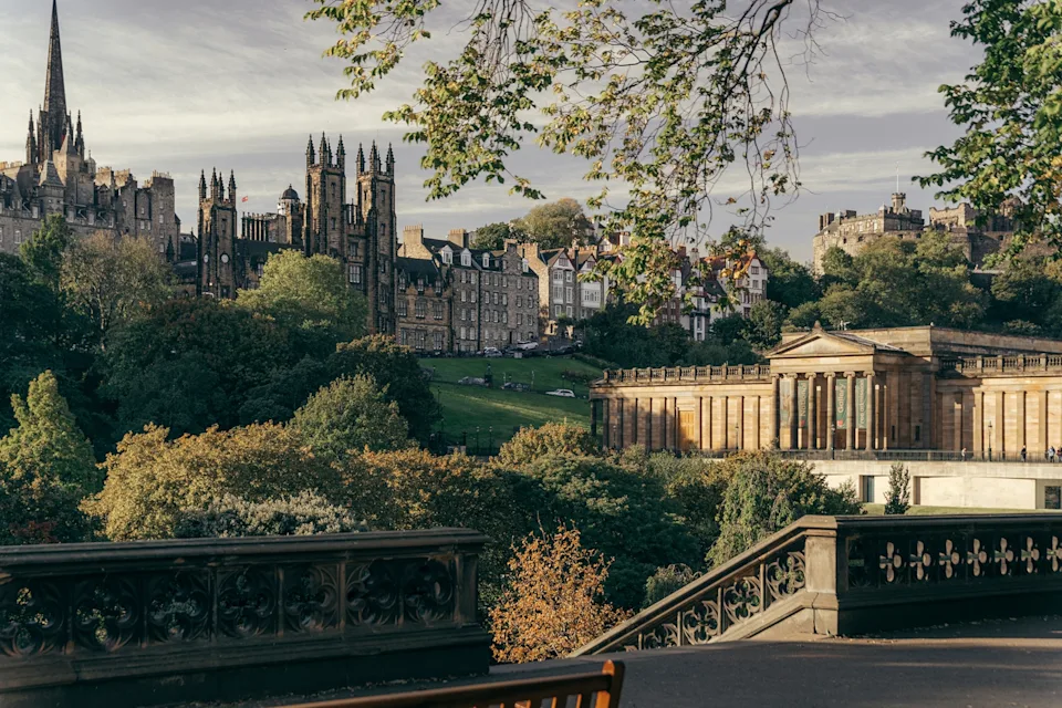 A scenic, urban view of a hill park with a stone-columned building and residential houses lining the horizon.