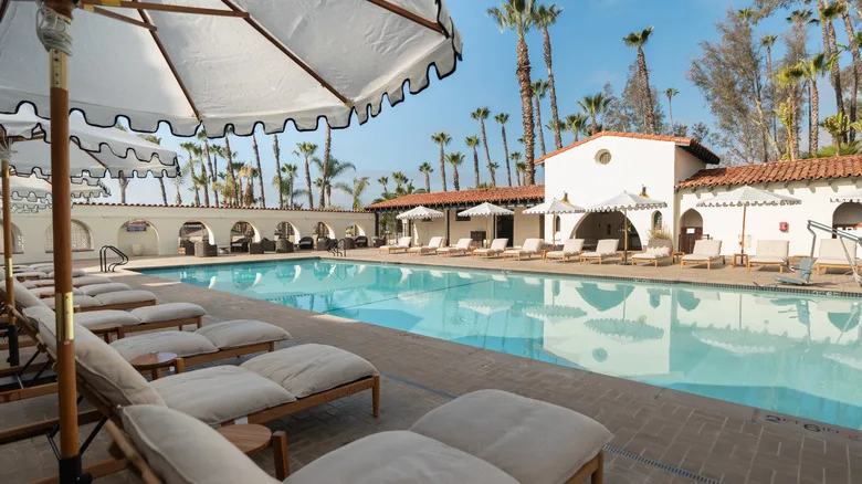 View of outdoor pool during the day with lounge chairs surrounding and trees in the background at Murrieta Hot Springs Resort
