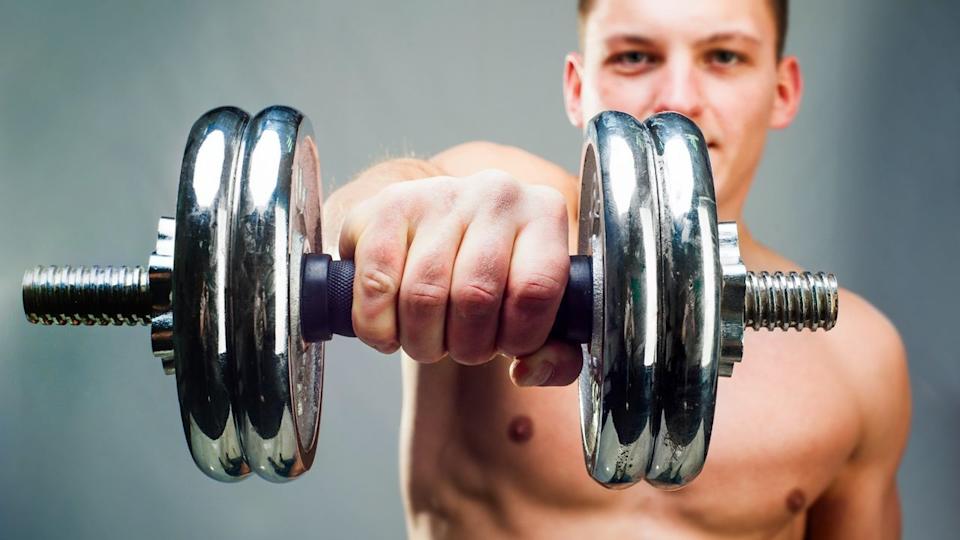  Man holding a dumbbell extended at shoulder height using an overhand grip close-up. 