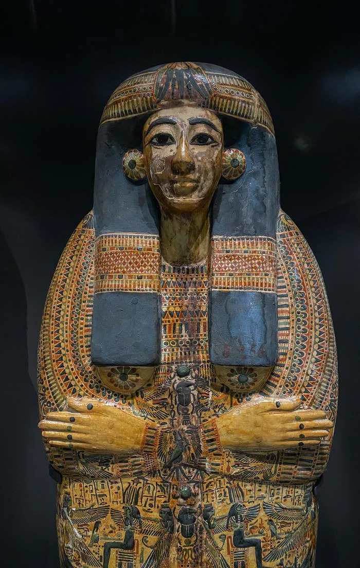 Ancient Egyptian sarcophagus with intricate, detailed patterns and a lifelike face, arms crossed over the chest