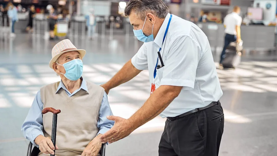 Airport employee talking to a senior tourist with a walking cane sitting in a wheelchair