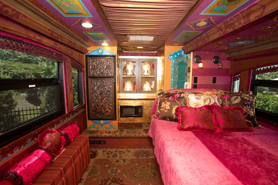 A tour bus bedroom with a bed covered in pink velvet and a cabinet of wigs against the wall 