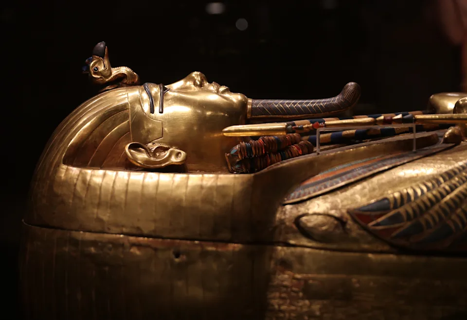Ancient Egyptian golden sarcophagus with intricate carvings and inlay, featuring a pharaoh's likeness, showcased in a museum exhibit