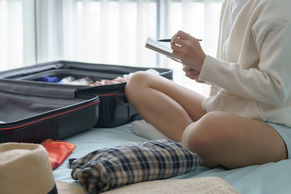 Asian girl preparing vacation in bedroom. Woman doing checklist before holidays trip.
