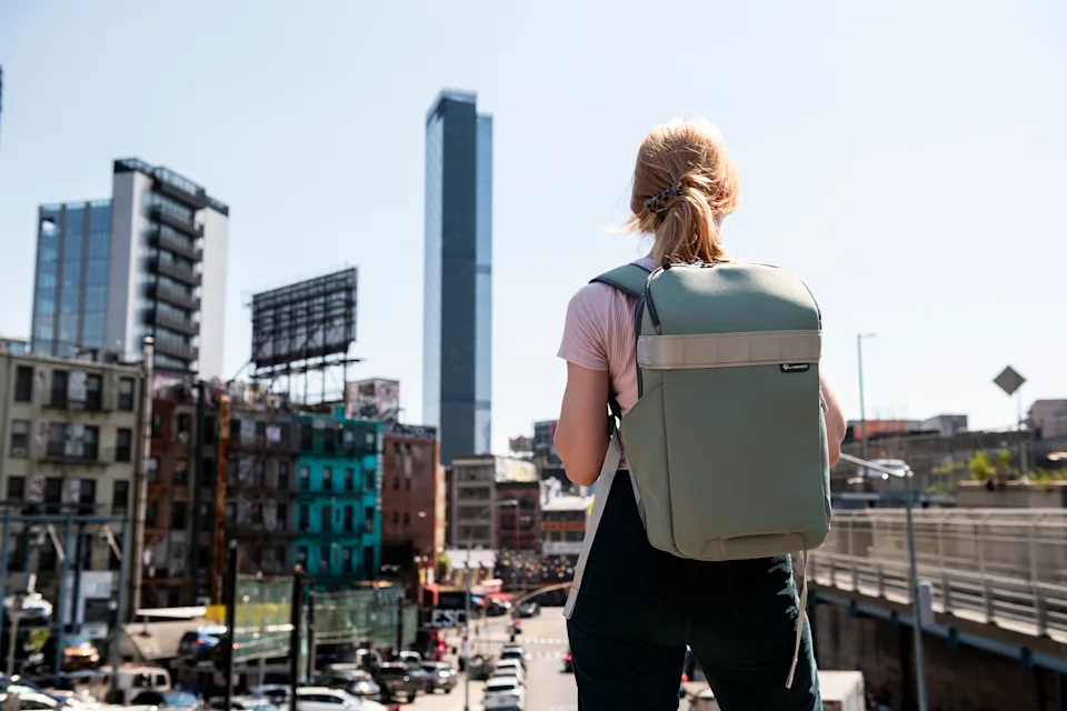 Woman stands in city with camera backpack on.
