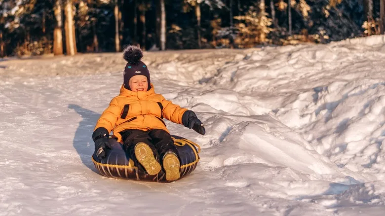 Toddler wearing a yellow jacket sliding down a hill on a snow tube
