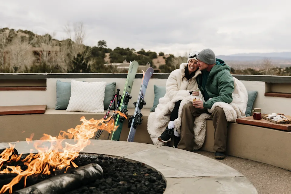 A couple warms by the fire after a day of skiing on the beautiful patio of Four Seasons Resort Rancho Encantado Santa Fe