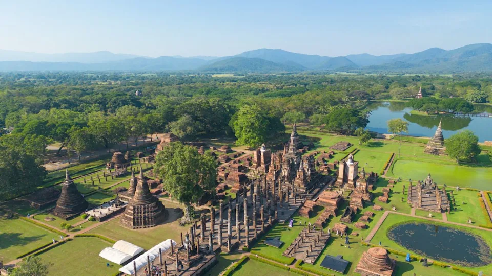Aerial view of Sukhothai Historical Park, buddha pagoda stupa in a temple, Sukhothai, Thailand with green mountain hills and forest trees. Thai buddhist temple architecture. Tourist attraction.