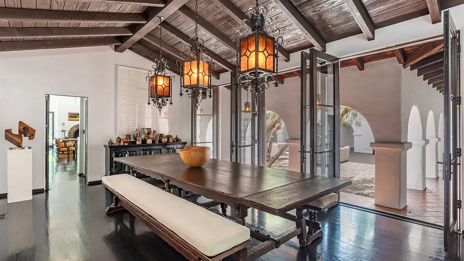 A dining room with floor-to-ceiling glass doors leading to the yard and unique lighting.