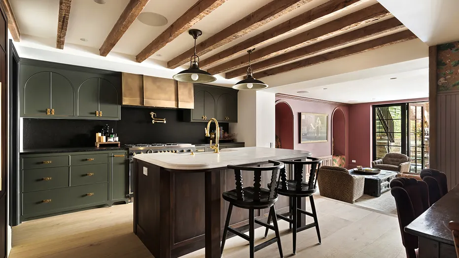 The kitchen features exposed wooden beams on the ceiling, an eat-in center island and green cabinets.