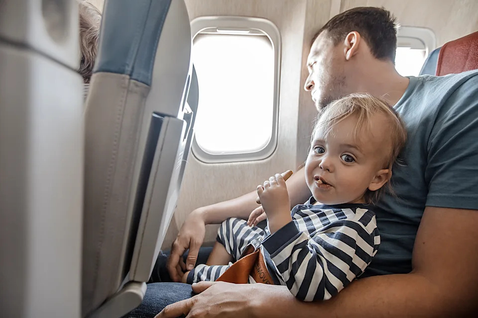 A baby sits on a man's lap on a plane
