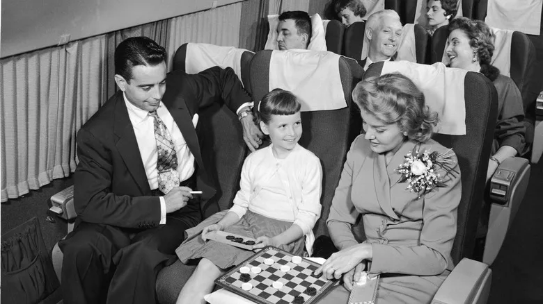 A man with a cigarette watches a woman and child play checkers on a flight