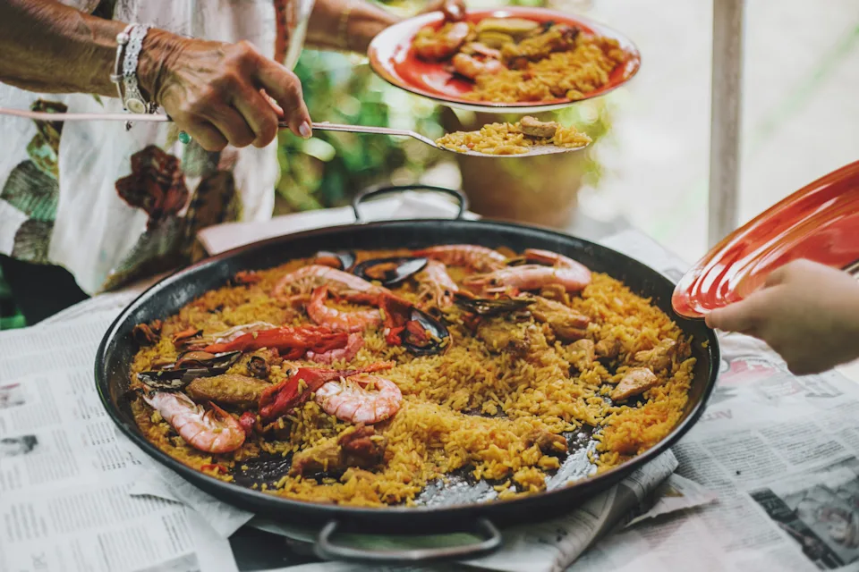 People serve seafood paella from a large pan on a table, highlighting a cultural dining experience