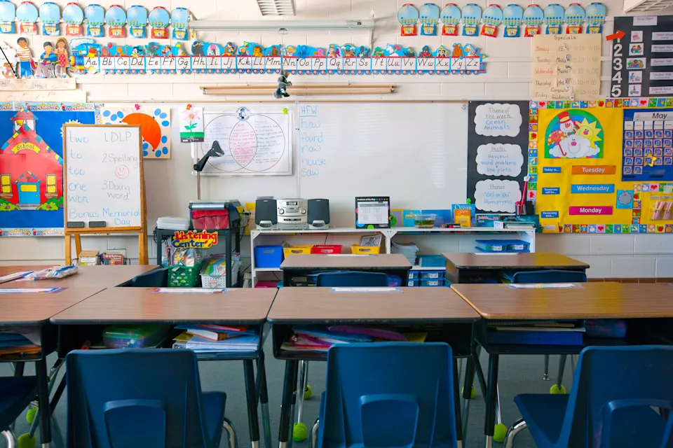 Classroom with neatly arranged desks and chairs facing a whiteboard, walls decorated with colorful educational posters and charts