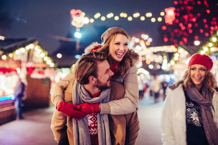 Young couple having fun outdoors at winter fair. Wearing warm clothes, hats and scarfs.
