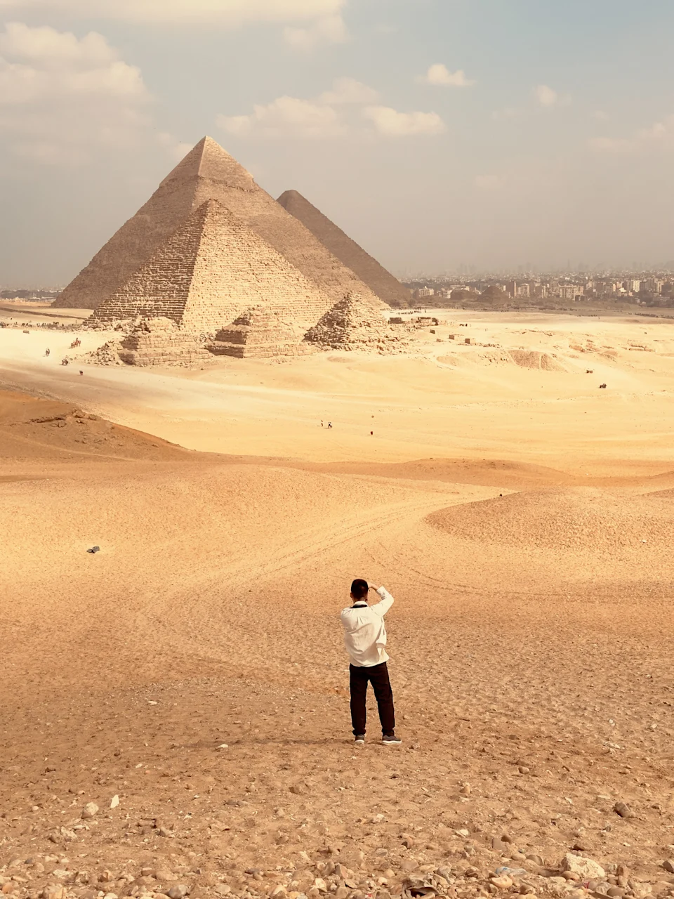 This photograph was taken on January 29, 2025, at the Giza Pyramids in Cairo, Egypt. The Giza Pyramids are a world - renowned complex of ancient tombs. Constructed during the Fourth Dynasty of the Old Kingdom in Ancient Egypt, they were built to house the remains of pharaohs. The most prominent ones are the Great Pyramid of Khufu, the Pyramid of Khafre, and the Pyramid of Menkaure. These colossal structures were crafted from massive stone blocks, some weighing tons, showcasing the advanced engineering and architectural skills of the ancient Egyptians. In the picture, a Chinese male tourist, around 40 years old, is seen exploring these majestic pyramids. he is photographing the pyramids, creating a memorable moment at this historical site.