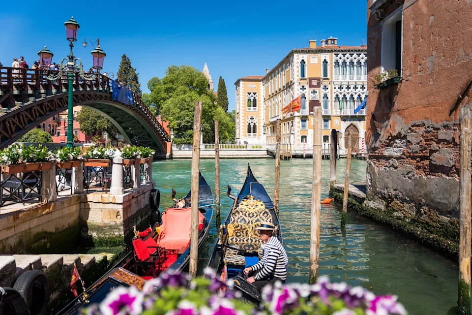 Gondolas float on a Venetian canal near a bridge, with historic buildings in the background, capturing the charm of Venice's waterways