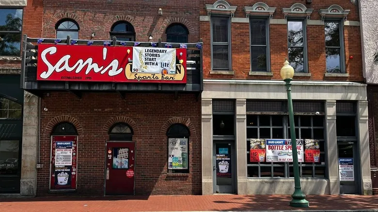 Front exterior of Sam's Uptown Cafe with a red restaurant sign hung on the balcony above