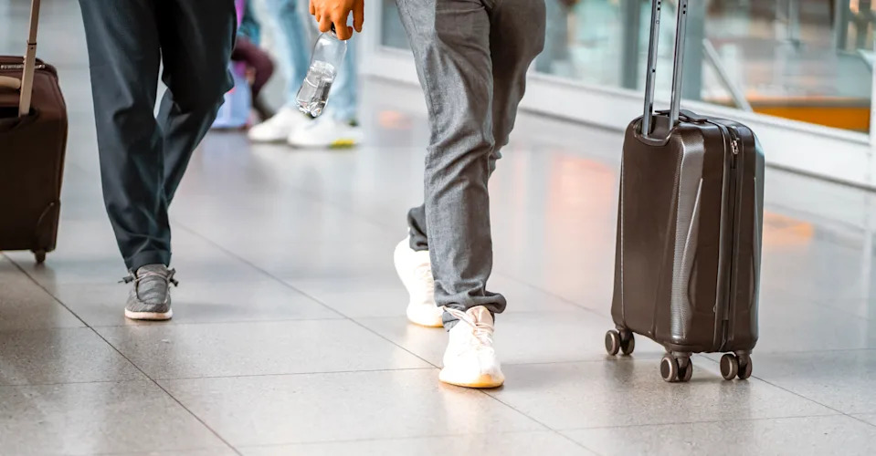Man with luggage is walking along airport corridor to gate and boarding, businessman traveling for work, close-up view of suitcase and legs.