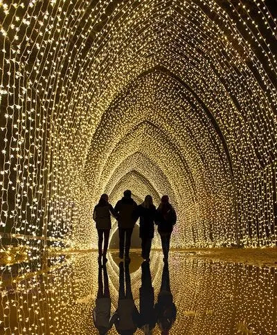 a group of four people walking through a tunnel with an arched top adorned with bright yellow lights