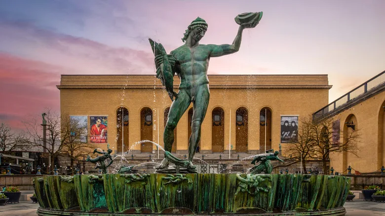 arched building entrance, green statue with fountain, people