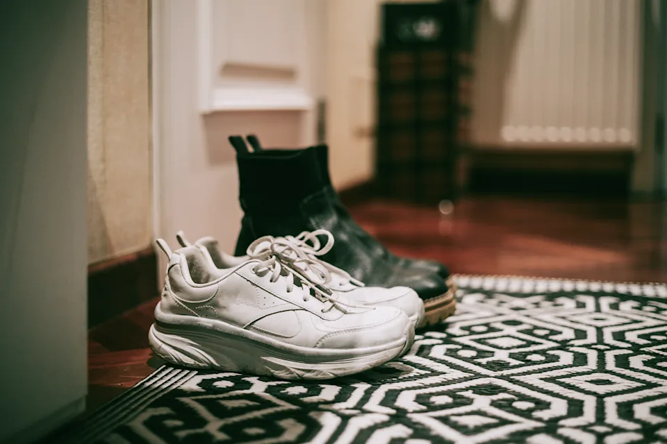 White sneakers and black boots placed on a geometric patterned rug near a doorway in a home setting
